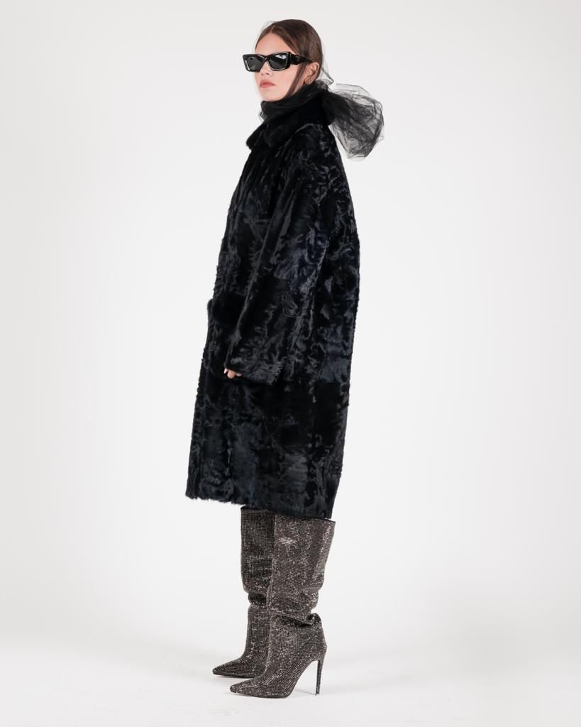 Donna con cappotto nero e stivali fantasia, di profilo, con occhiali da sole.