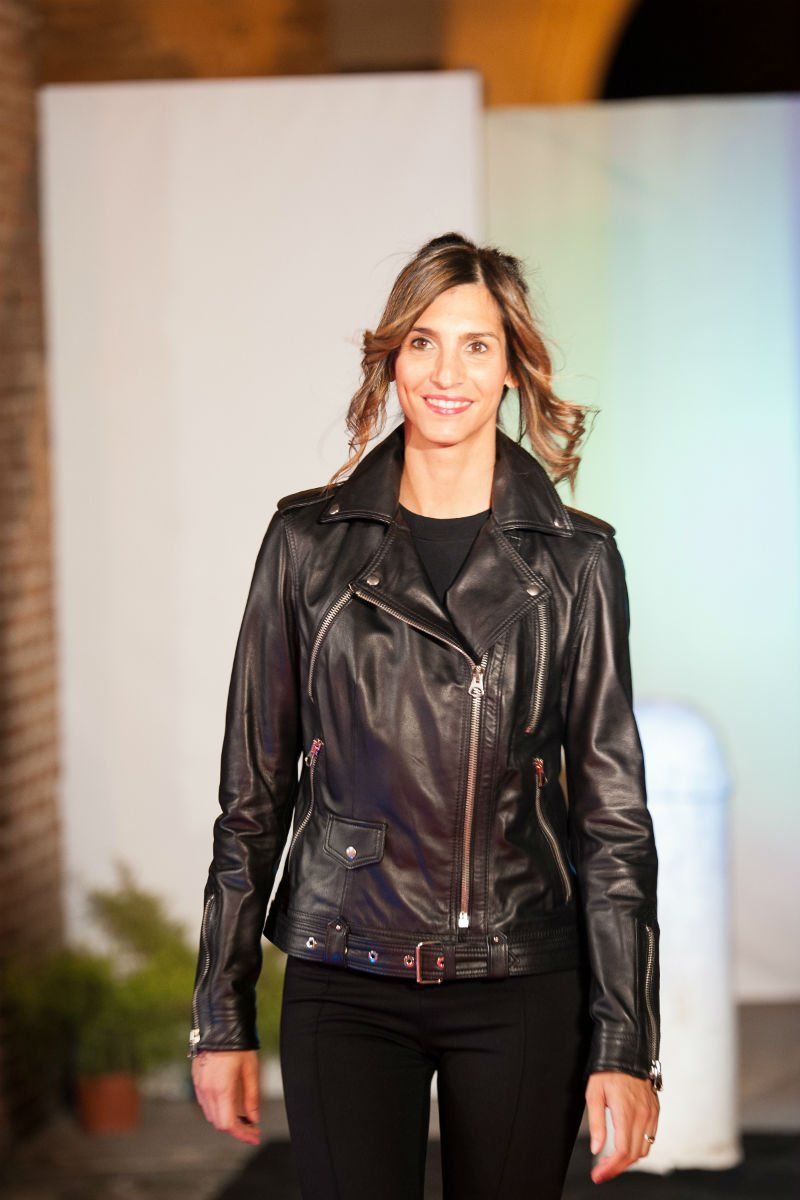 Donna che indossa una giacca di pelle nera e pantaloni neri, sorridente, in piedi su un palco.