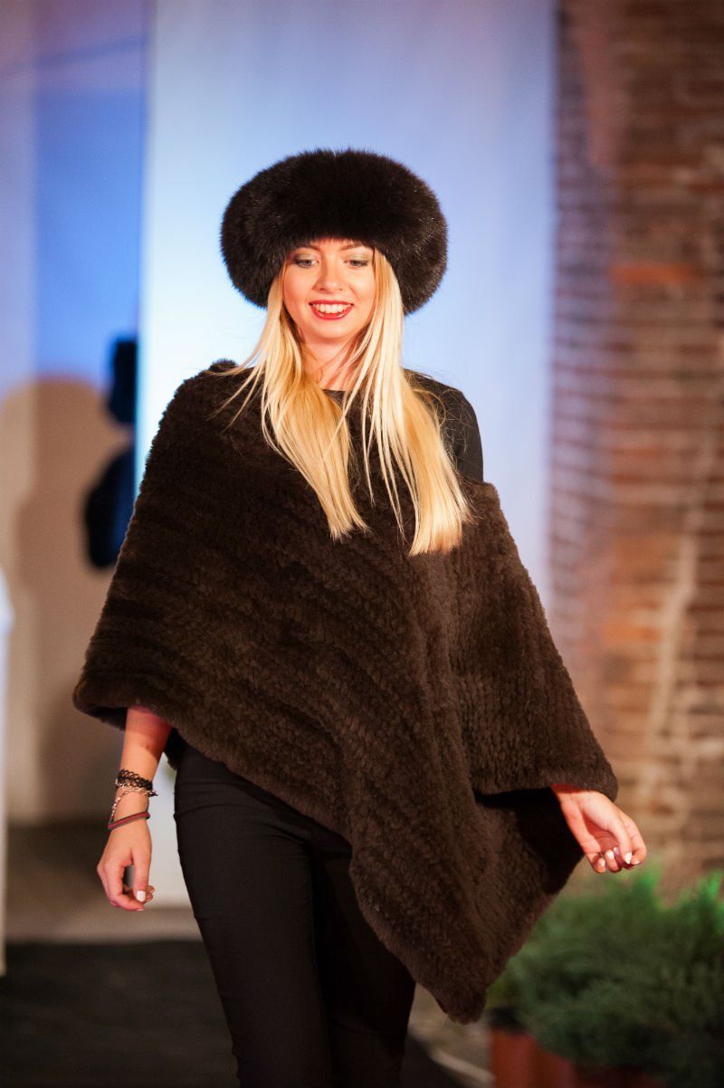 Donna con cappello di pelliccia marrone e poncho, pantaloni neri, sorrisi.