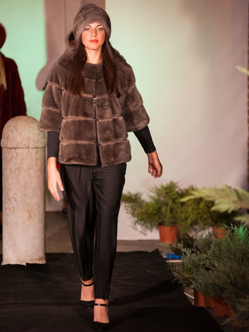 La donna indossa un cappotto di pelliccia marrone, un cappello, pantaloni neri, tacchi e sfila in passerella.