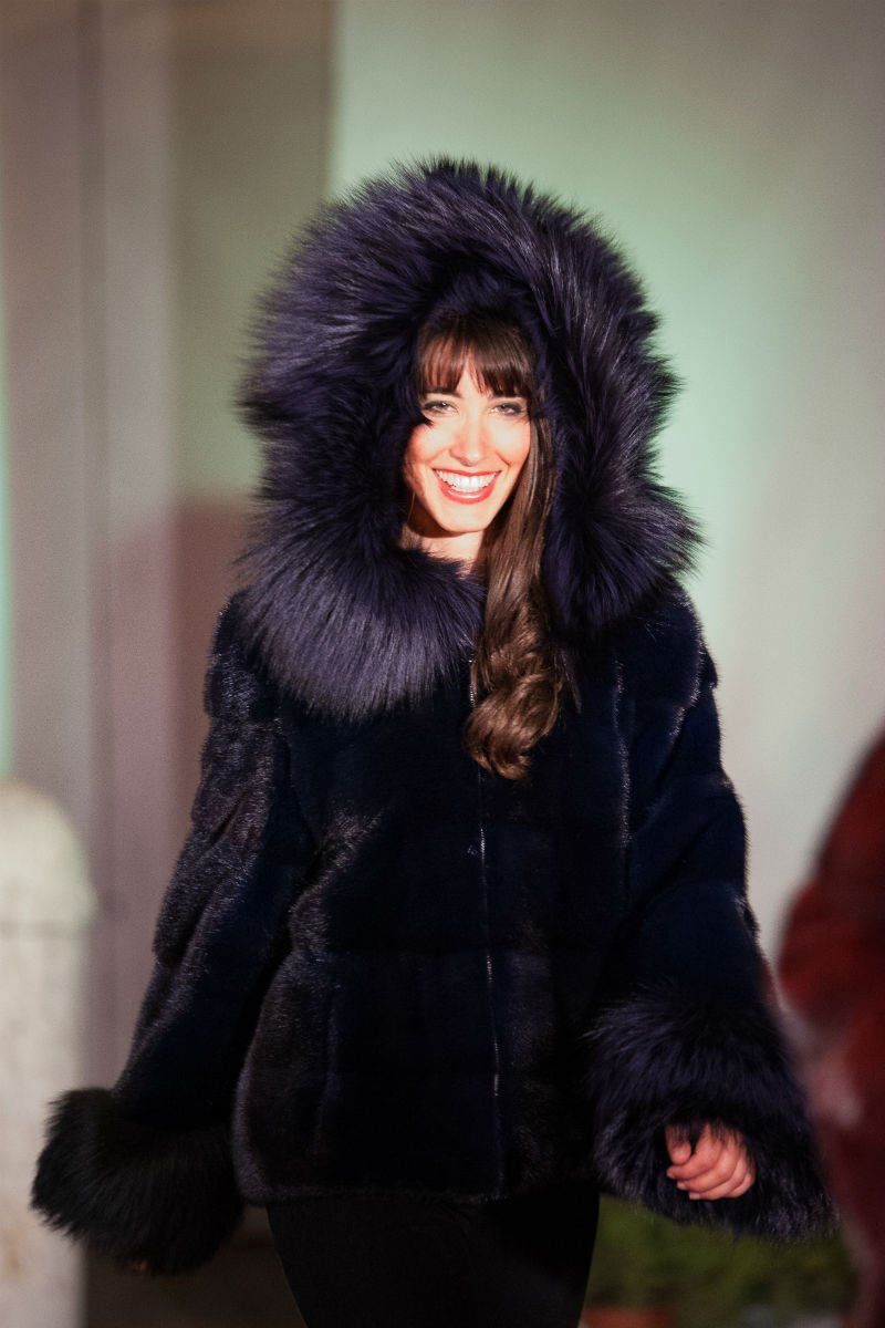 Donna sorridente che indossa un cappotto di pelliccia blu scuro con un grande cappuccio.