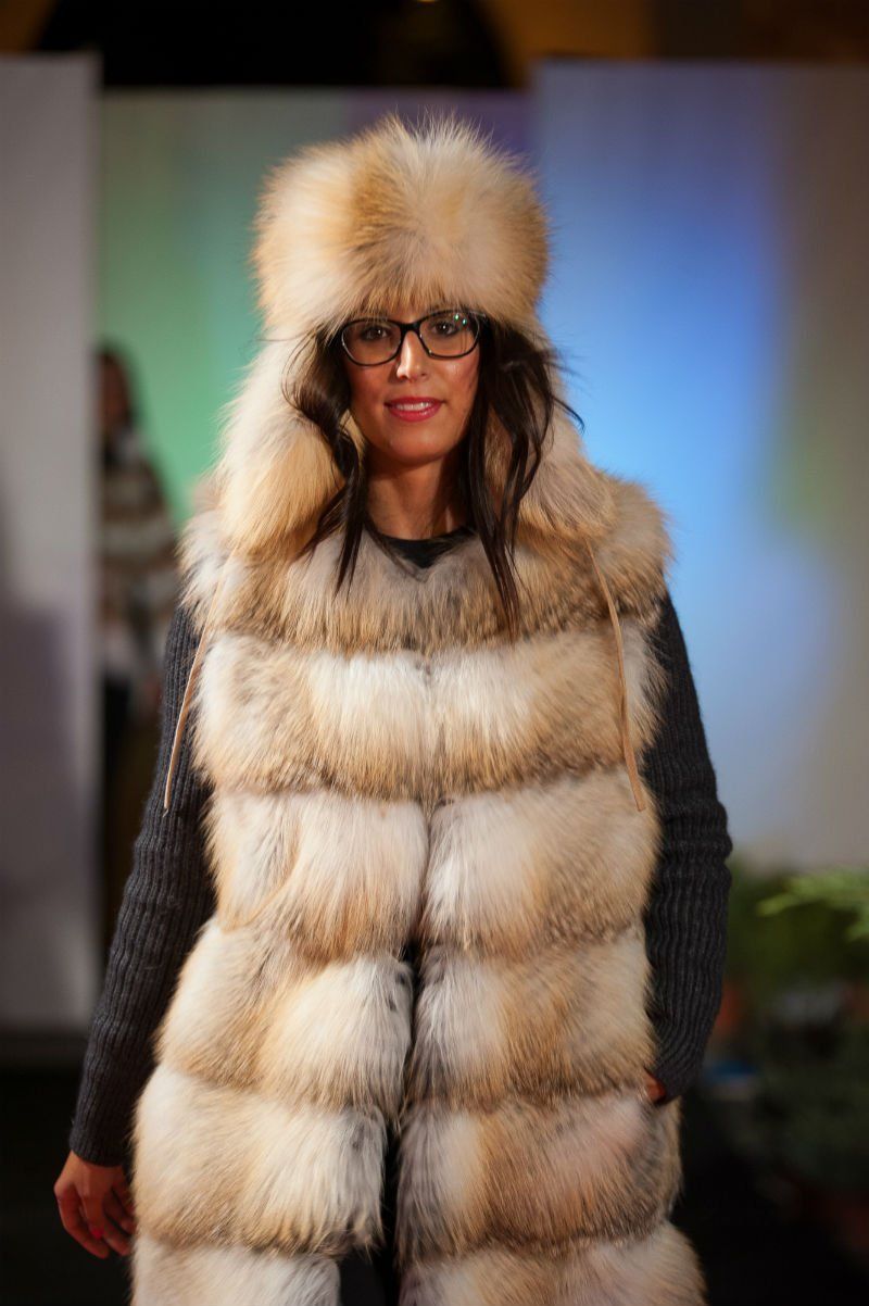 Donna sorridente che indossa un gilet di pelliccia e un cappello, in piedi su una passerella.