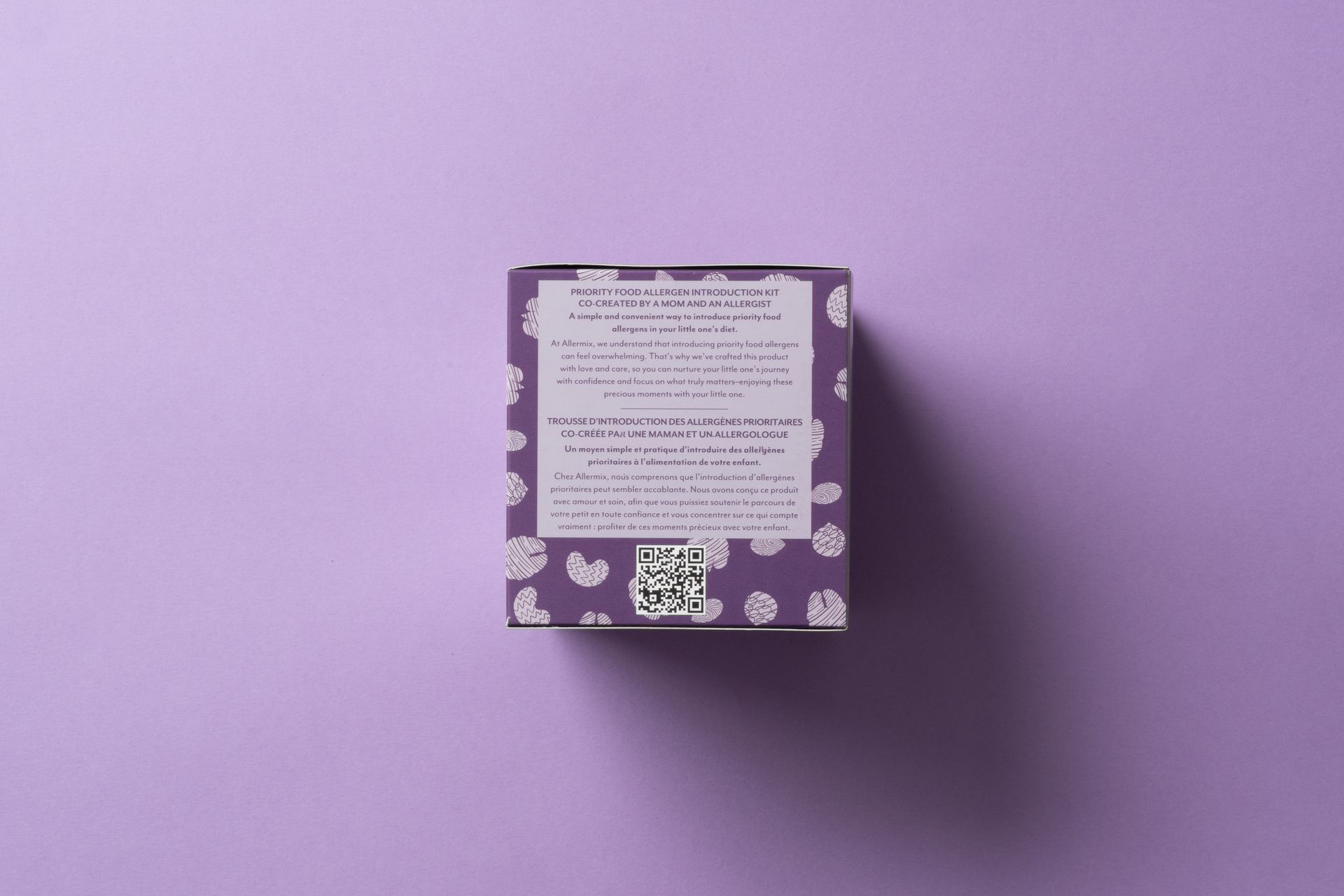 Small purple patterned box with a white label, centered on a lavender background.