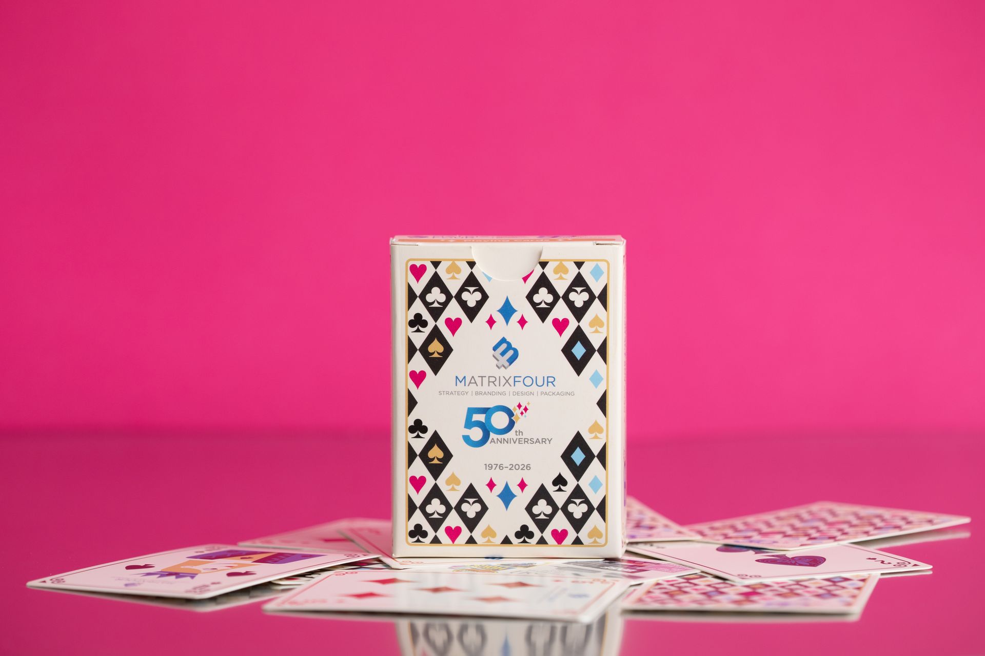 Playing cards arranged around a white deck box on a bright pink background
