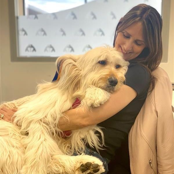 A woman is hugging a white dog in front of a window.