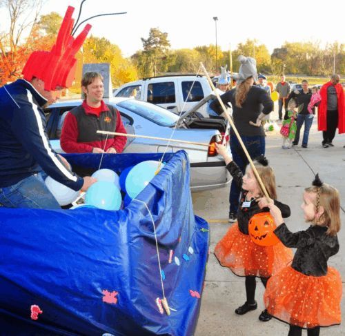 Children fish for balloons at a Halloween trunk-or-treat. Costumed kids use fishing poles.
