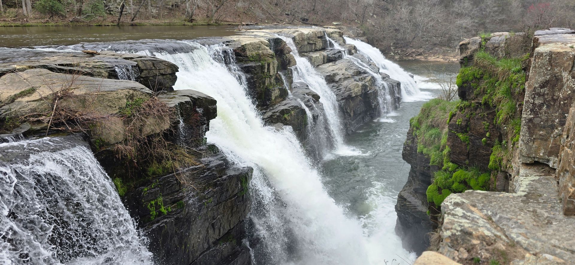 A waterfall is surrounded by rocks and trees in the middle of a river.