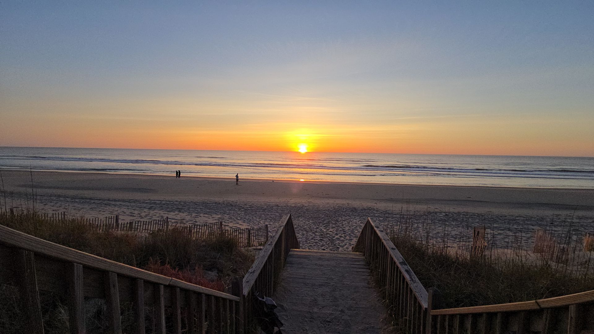 A wooden walkway leading to the beach at sunset.