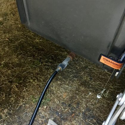 A black hose is attached to a metal object on the ground.