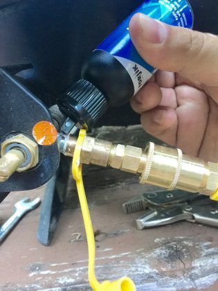A person is holding a bottle of oil and applying it to a hose connector.