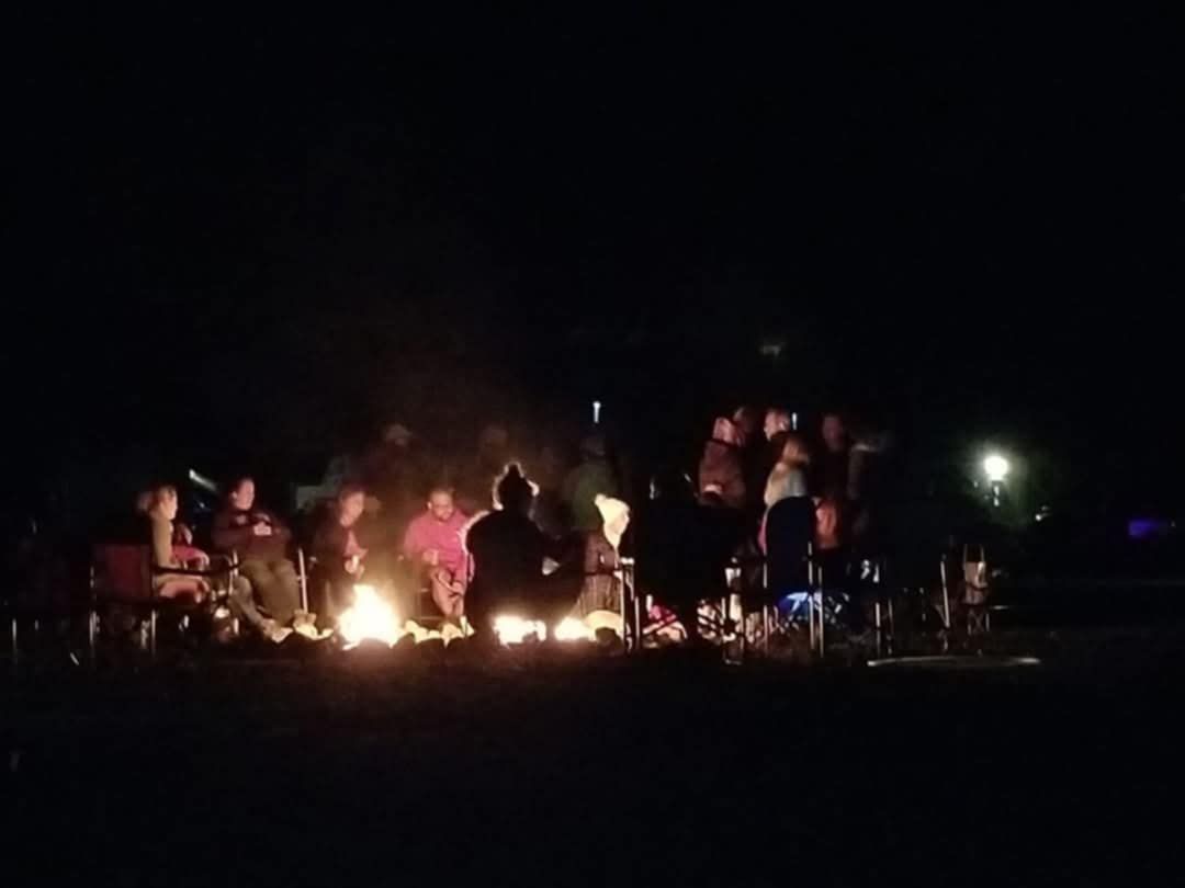 Group of people gathered around a bonfire at night, silhouetted in the light.