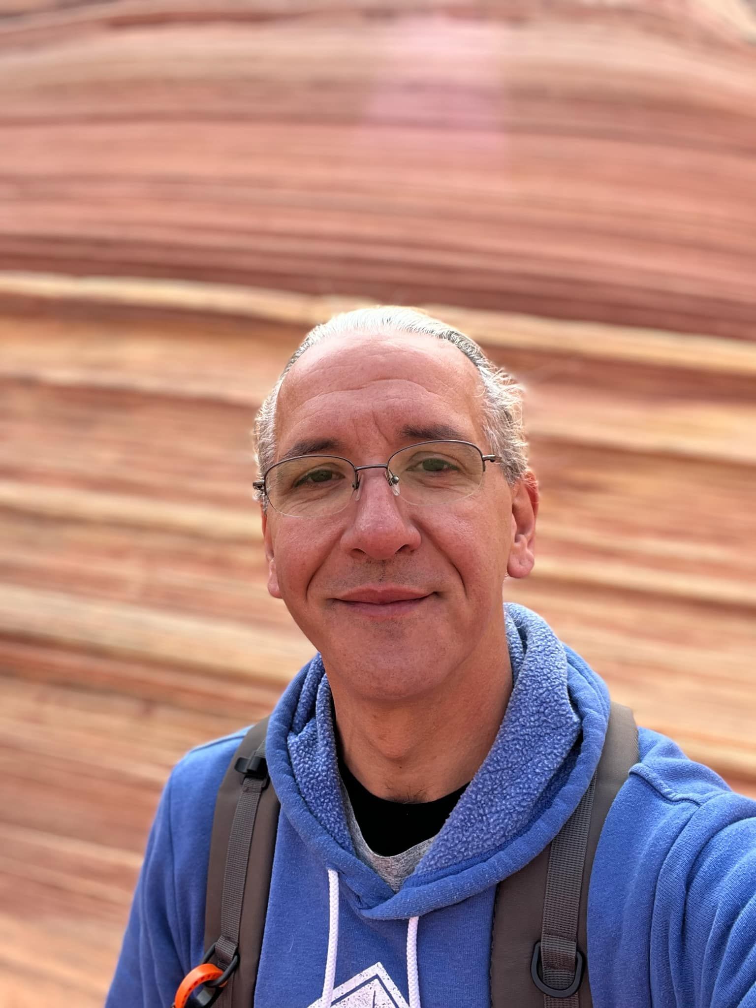 Man in glasses and blue hoodie in front of layered red rock formation.