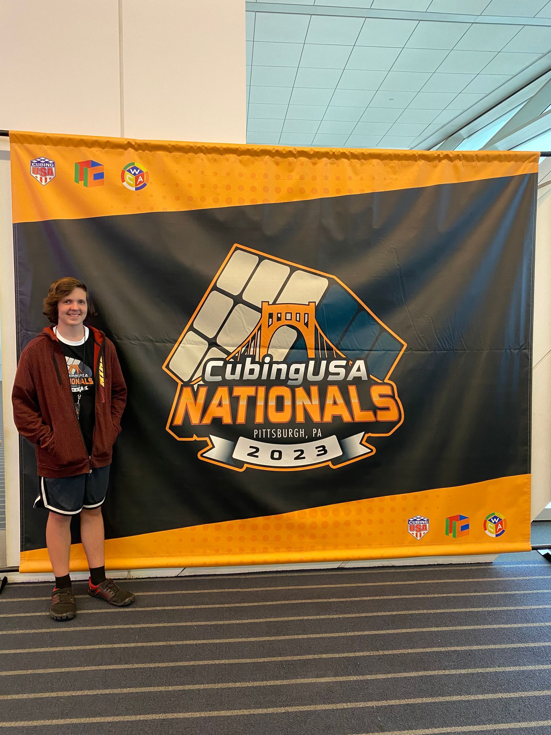 Person standing beside a large “NATIONALS” event banner in a convention hall.