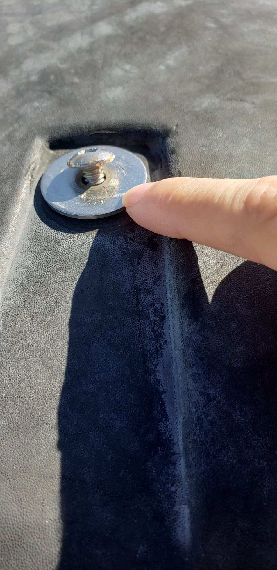 Finger pointing at a small metal fastener on a dark fabric surface on rv roof with gap in sealant