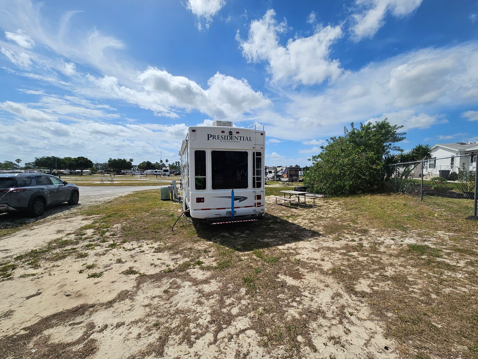 White van parked on a sandy lot under a bright blue sky with scattered clouds.