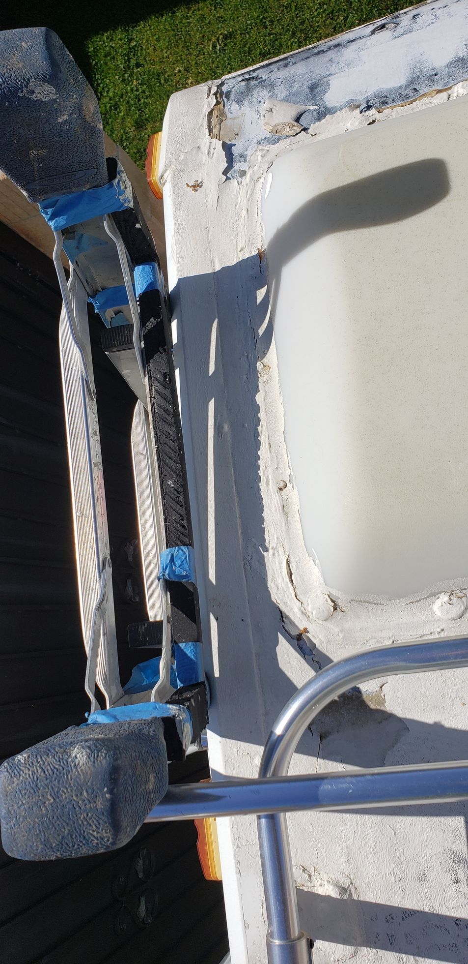Blue ladder beside a white boat hull with a black rope or hose on a dockside surface