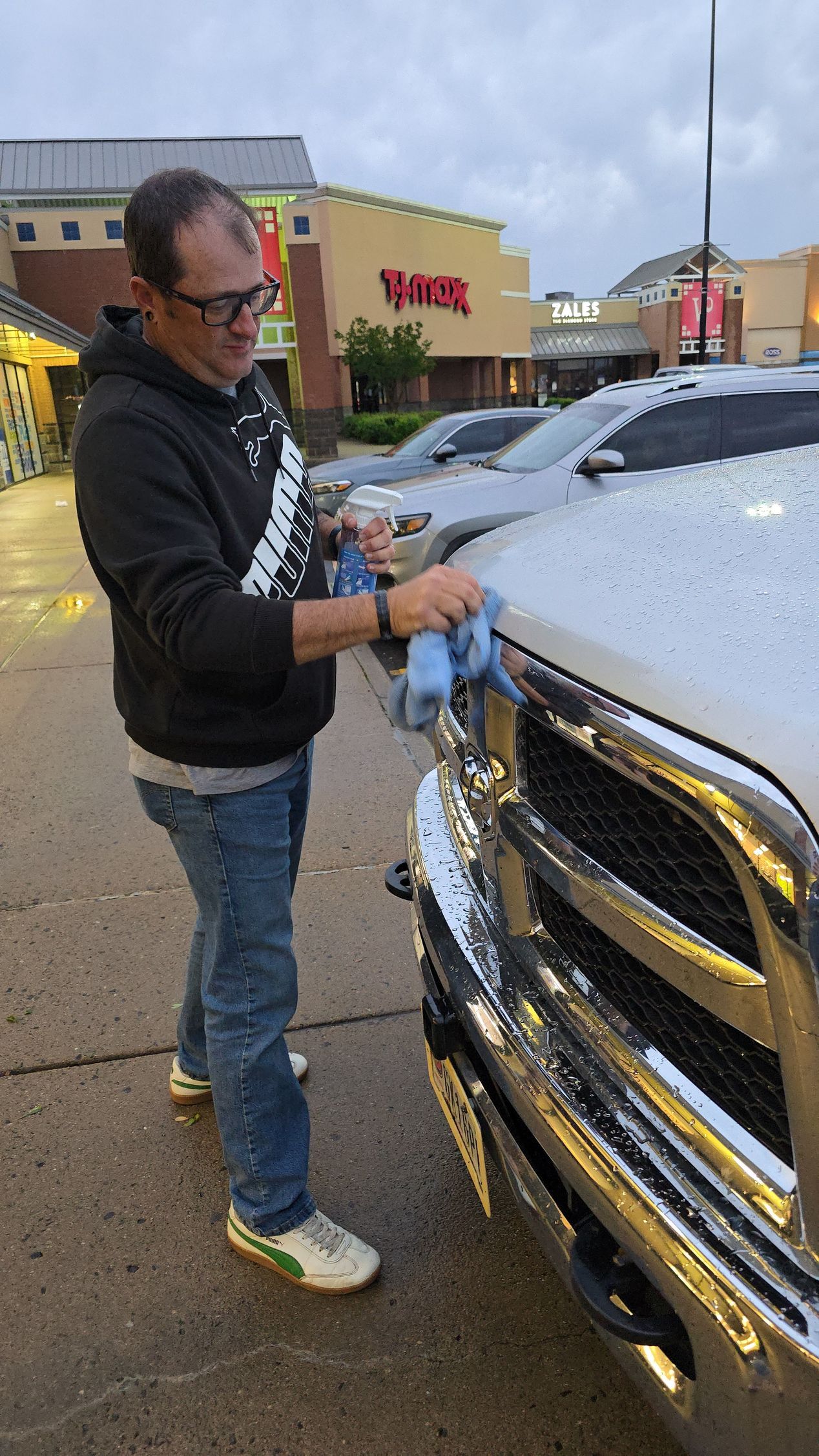 A man is cleaning the front of a silver truck in a parking lot.