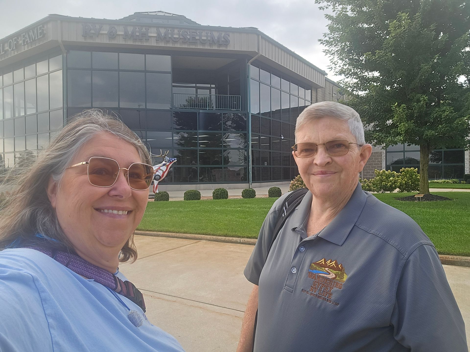 Two people smiling in front of a modern glass building on a sunny day