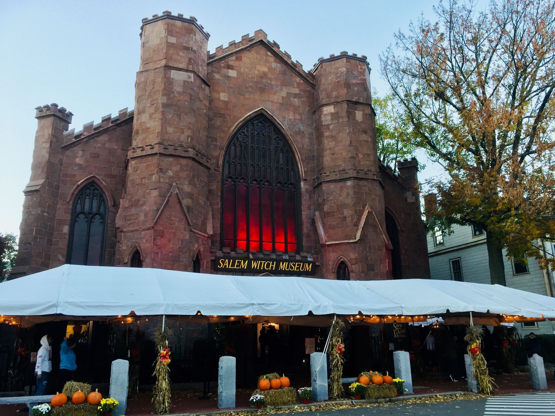Brick building with large arched windows, under a white tent decorated with pumpkins; 