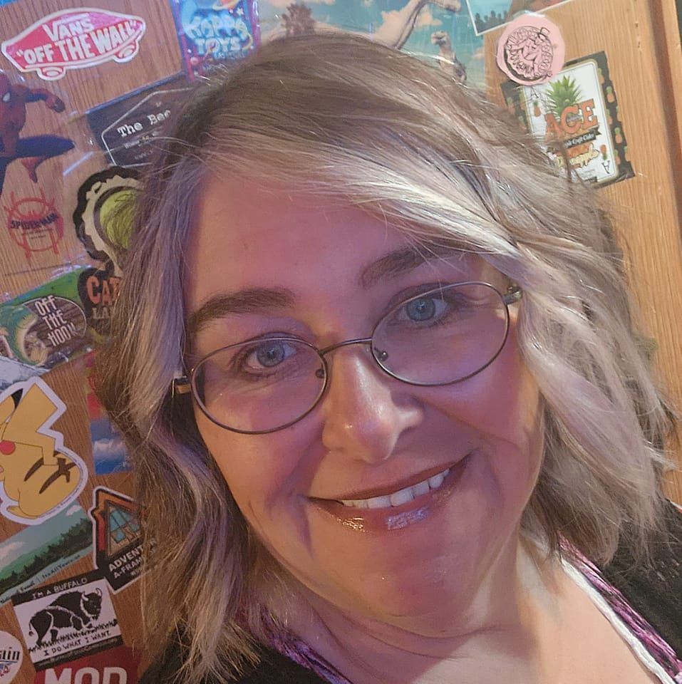 Woman with glasses smiles; silver and brown hair; stickers on wooden background.