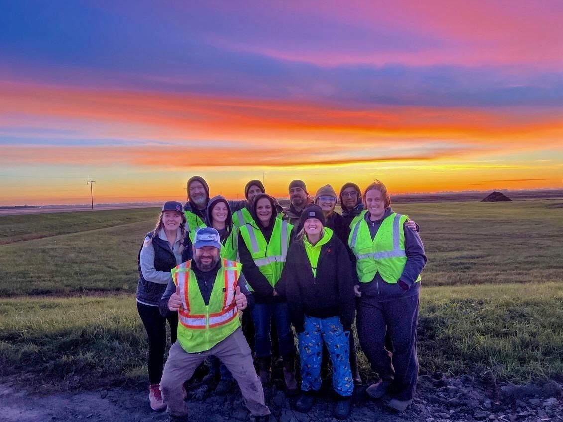 A group of people are posing for a picture in a field at sunset.