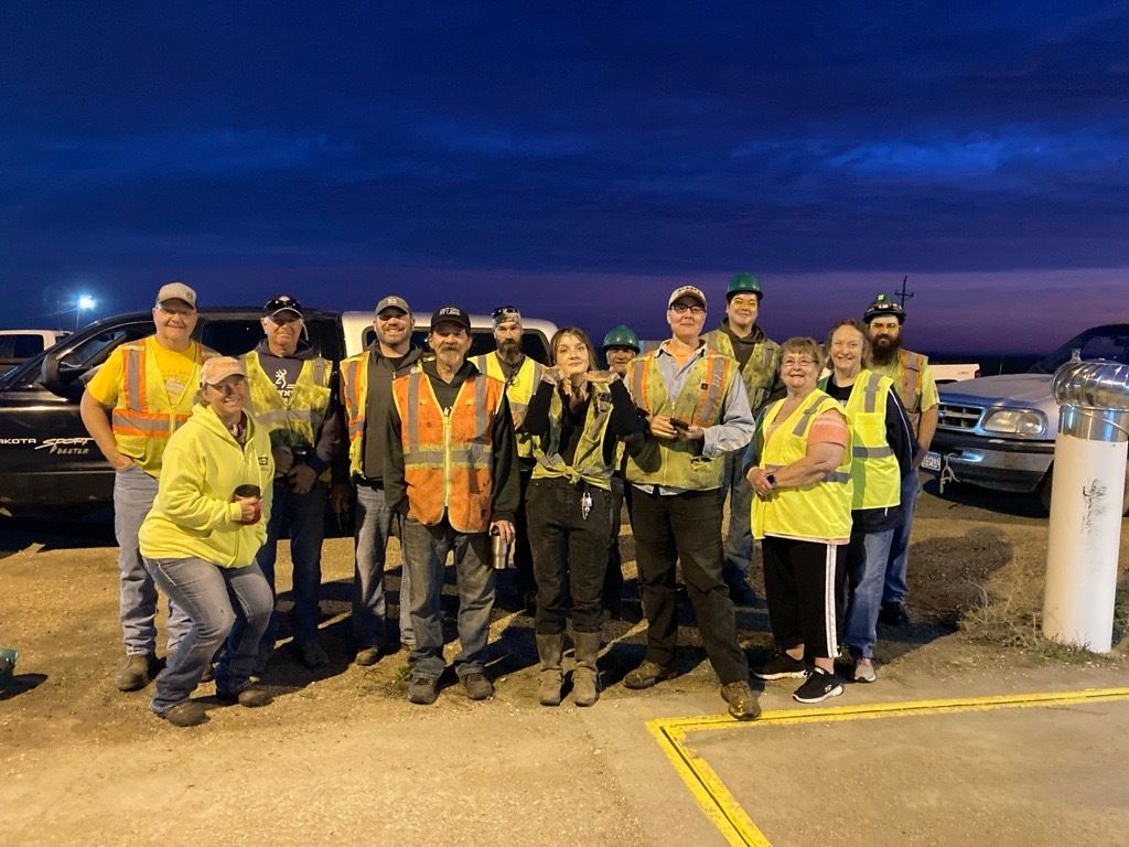 A group of people wearing safety vests are posing for a picture in a parking lot.