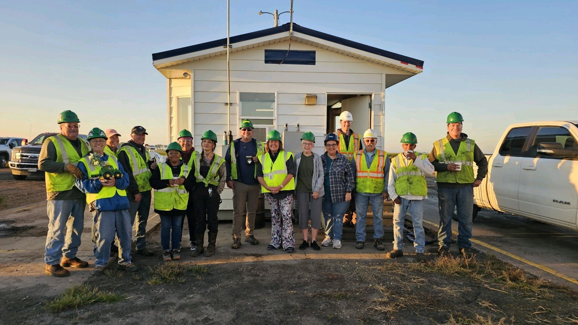 A group of construction workers are posing for a picture in front of a small building.