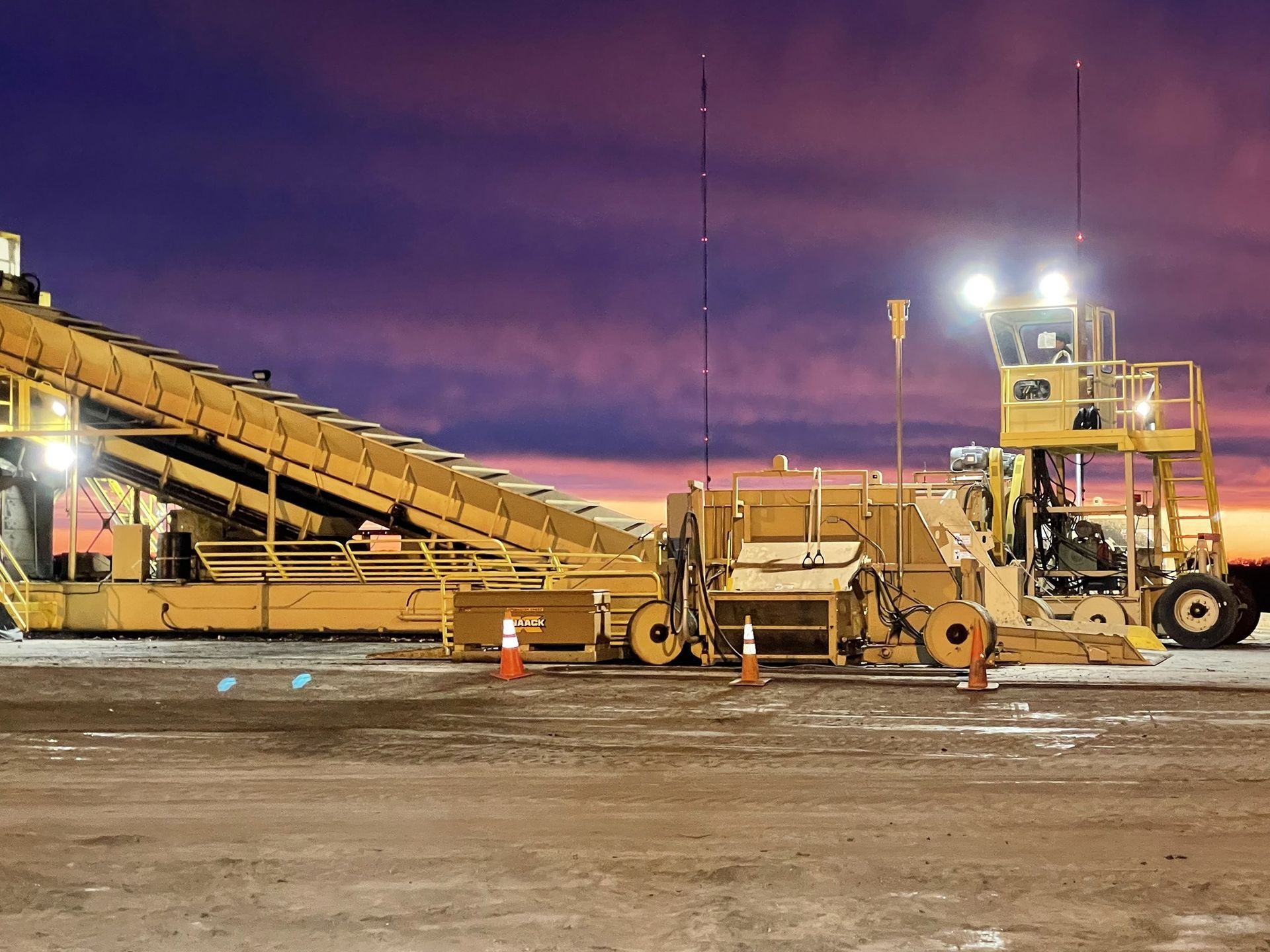 A large yellow machine is parked in a parking lot at night.
