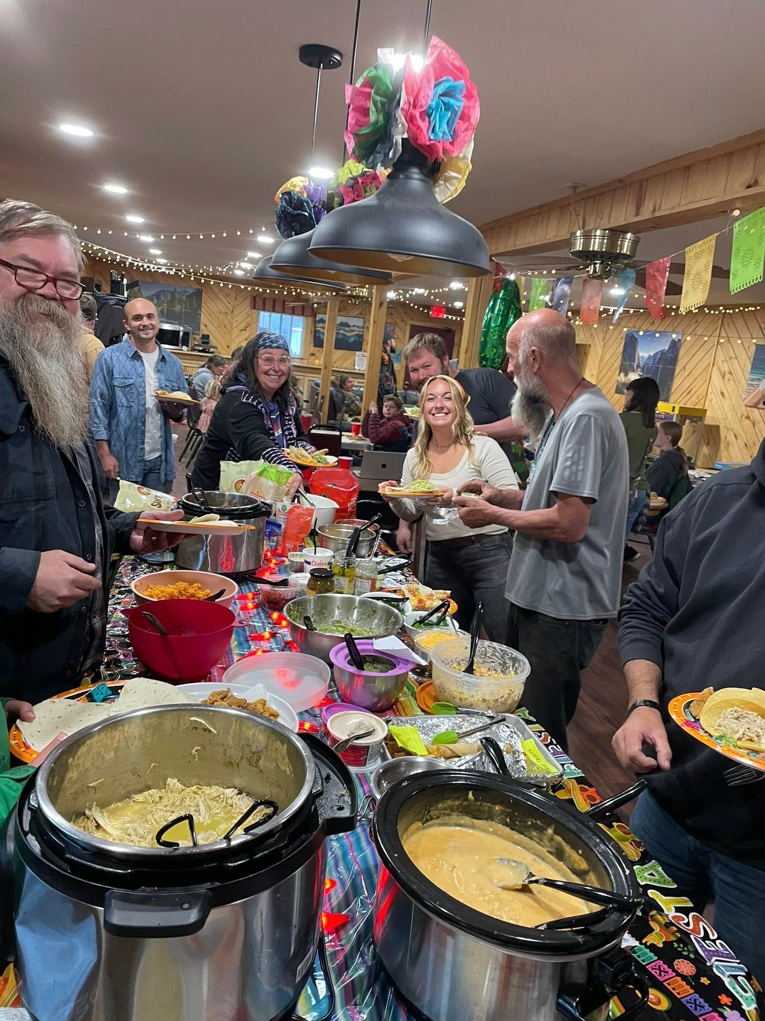 A group of people are standing around a table with pots of food.