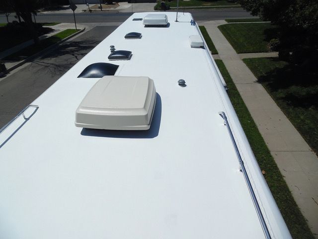 White RV roof with vents and air conditioning units, viewed from above, with residential street in the background.