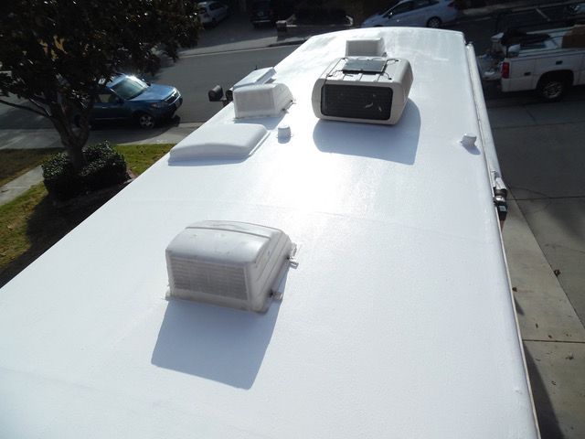 White RV roof with air vents and air conditioning unit, parked on a street.