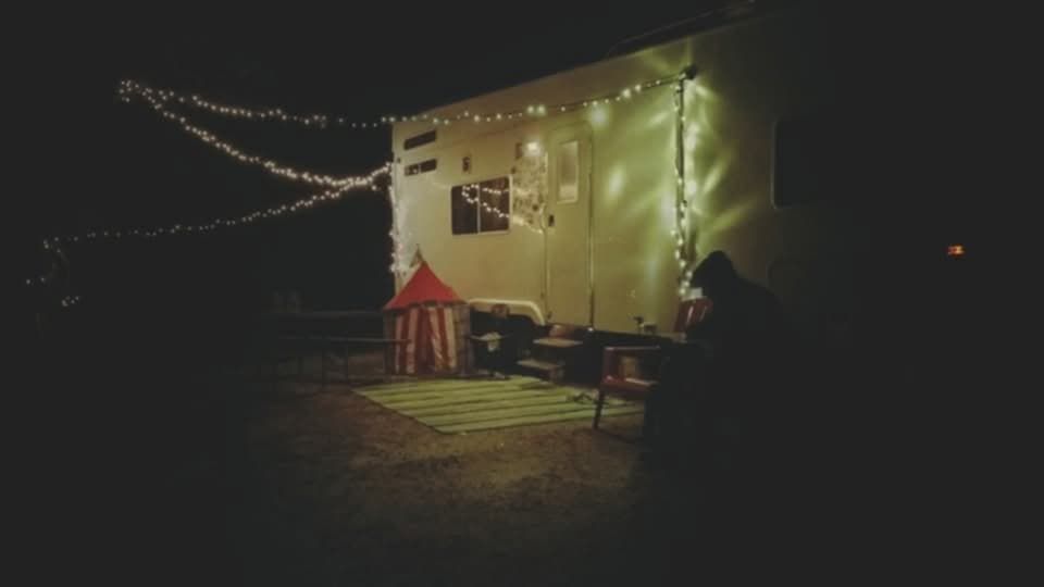 RV exterior at night with string lights, a small tent, and an armchair.