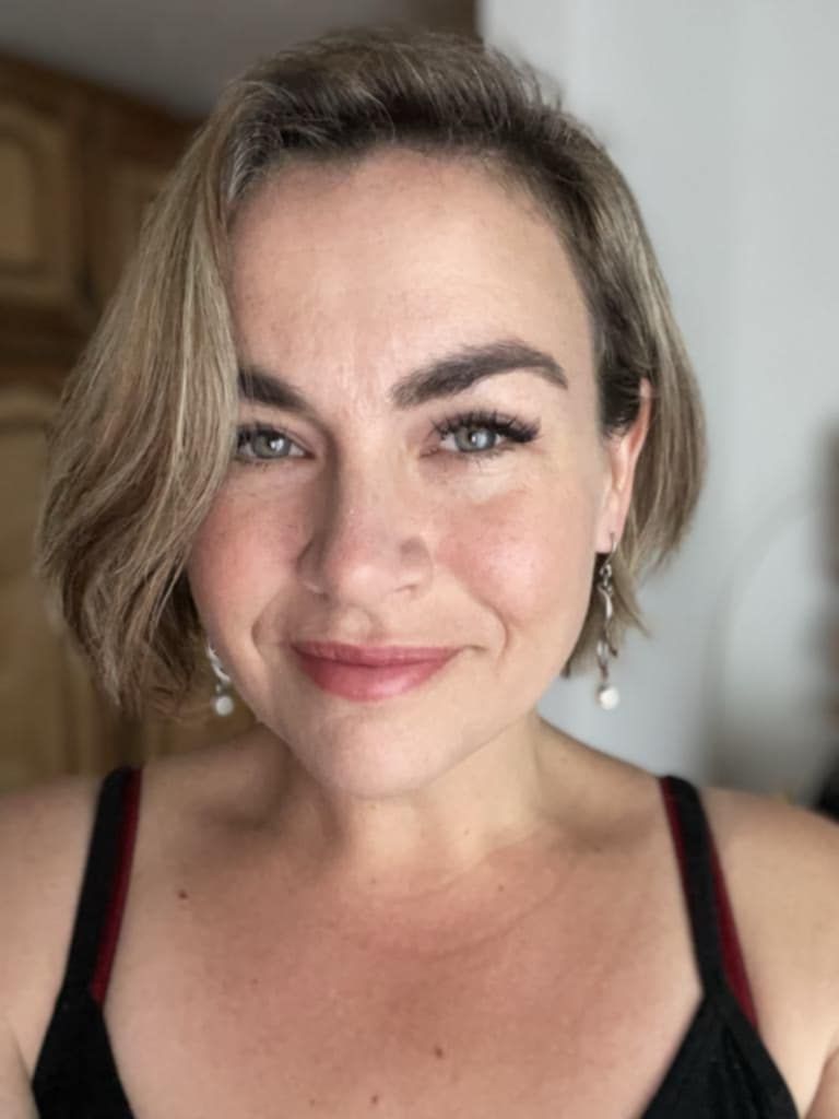 Woman with short blonde hair and earrings smiles at the camera, wearing a black top.