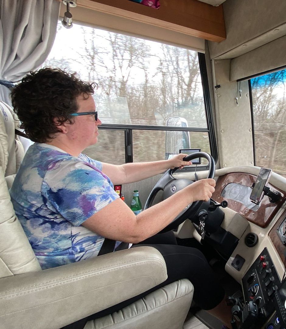 A woman is sitting in the driver 's seat of a rv holding the steering wheel.