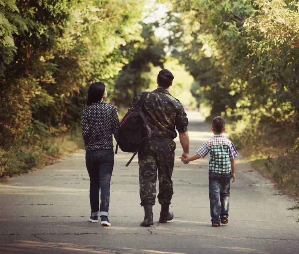 Family, soldier in uniform, holding hands, walking down a road with trees.