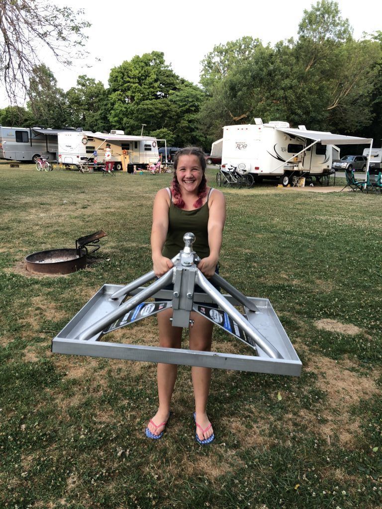 A woman is holding a trailer hitch in a field.