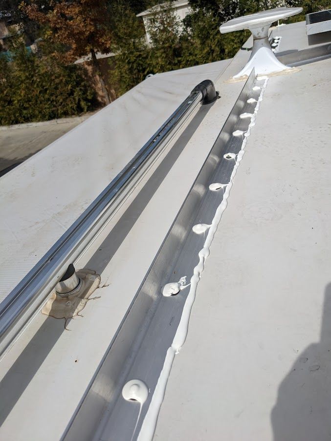 A flat, white roof with a long metallic channel containing round, white caps and a vent.