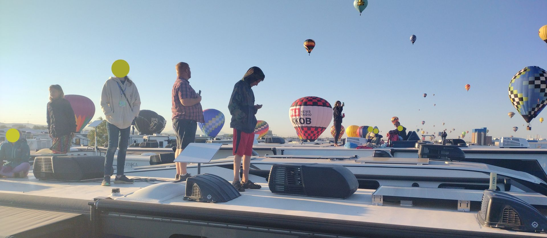 People watching hot air balloons. The sky is blue.