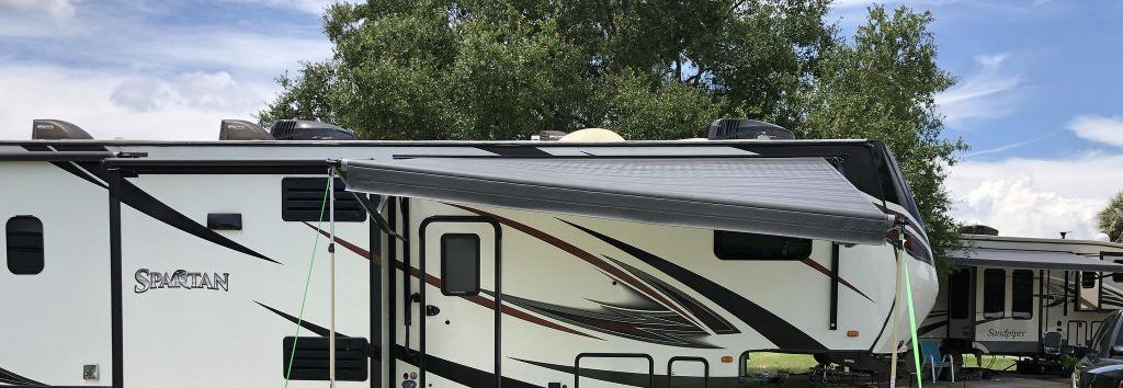 A white rv with a black awning is parked in front of a house.