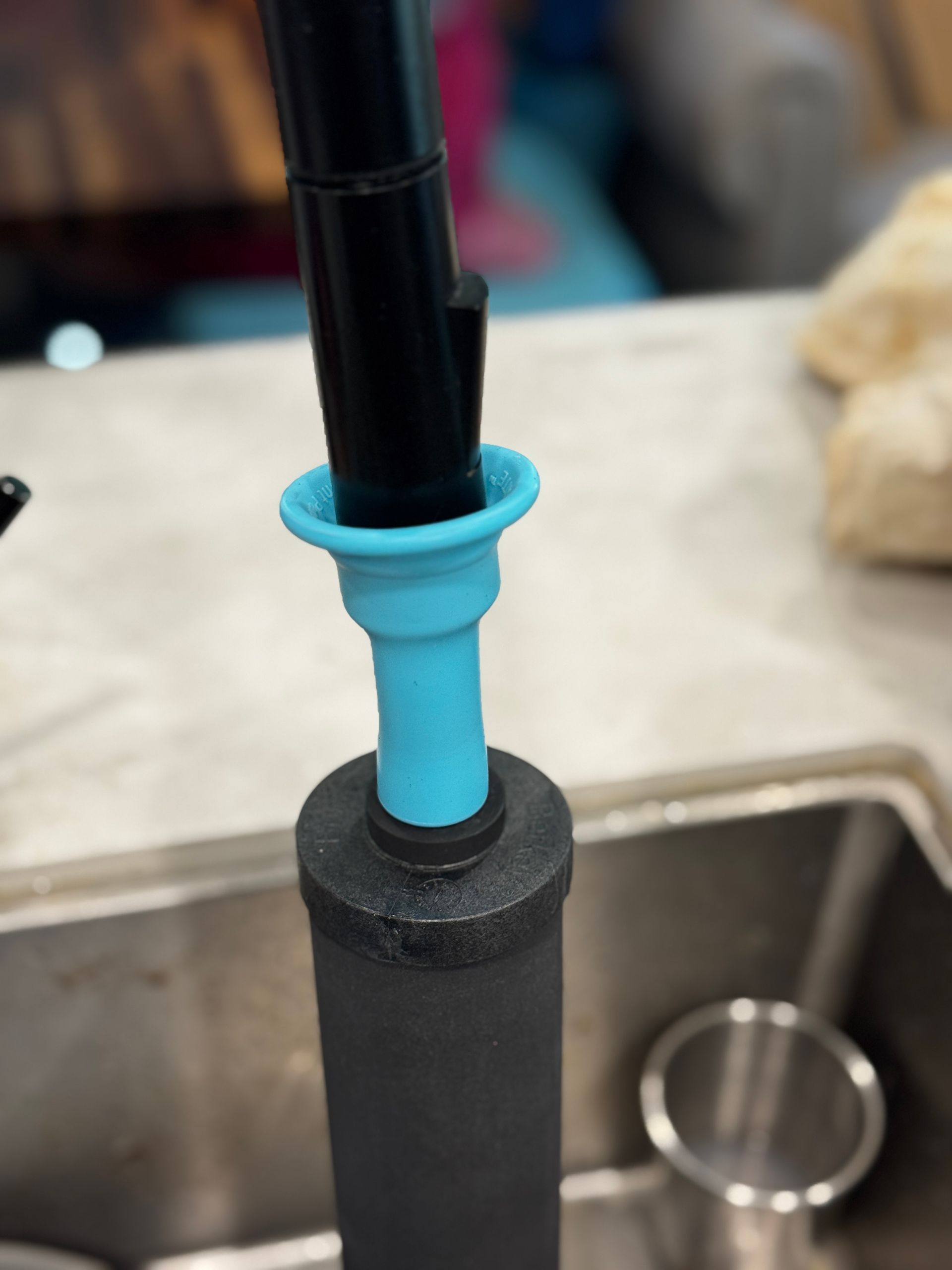 Blue silicone adapter connected to a black filter and faucet in a kitchen sink.
