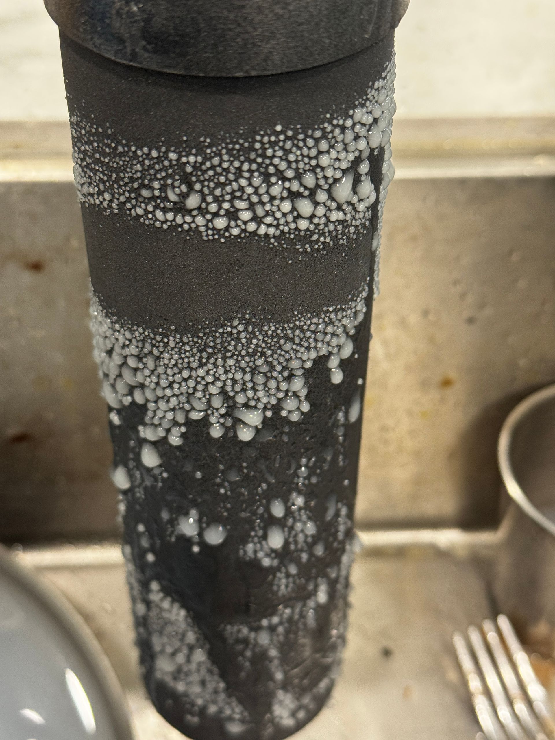 Black pipe with white condensation forming droplets in a sink.