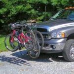 Silver truck with three bikes mounted on a front-end hitch, parked outdoors.