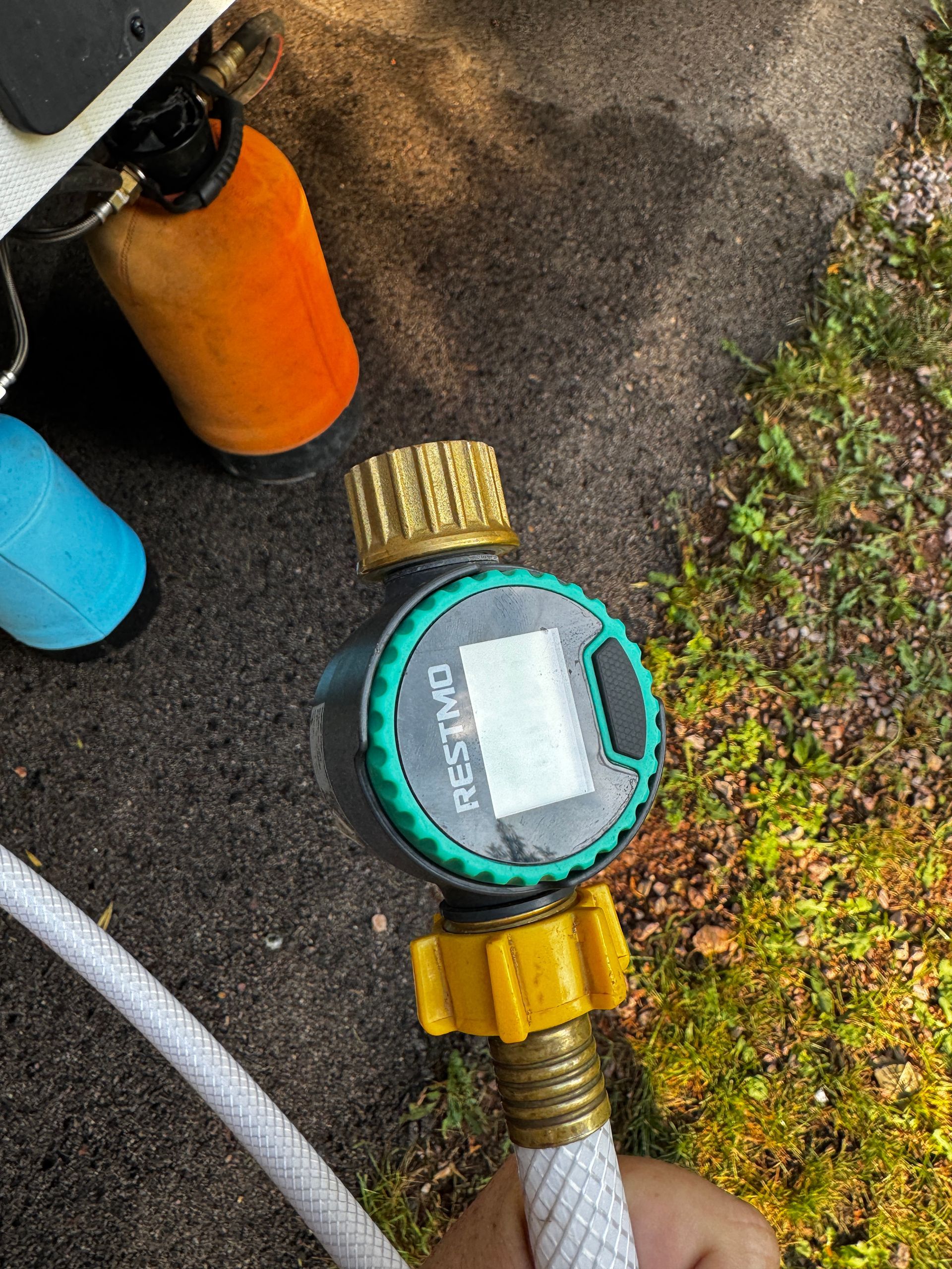 A green and black timer with an LCD screen is connected to a white hose.