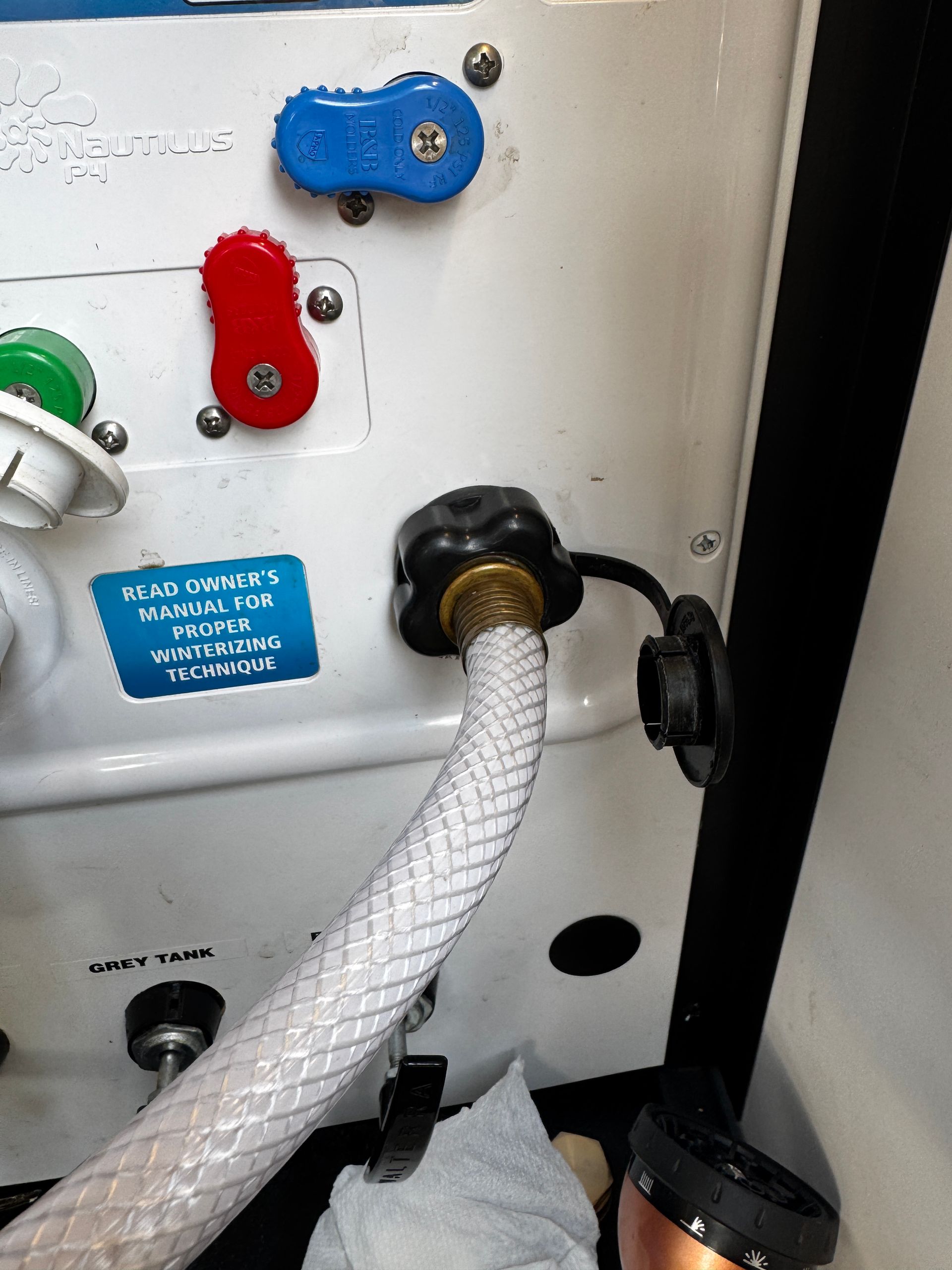 White RV water hookup with a hose connected to a black valve and blue, red, and green caps.