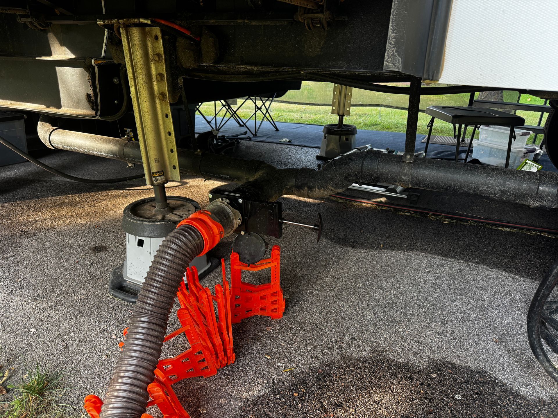 RV sewer hose connected, angled downward, on concrete, jack stands support the undercarriage.