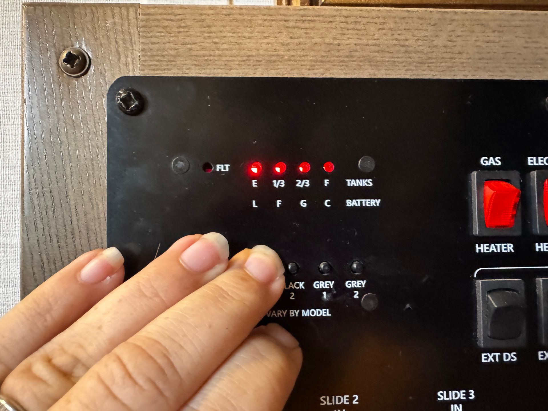RV control panel with red lights, finger pressing a button.