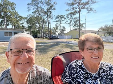 Smiling couple seated outdoors; sunny day, trees in background.