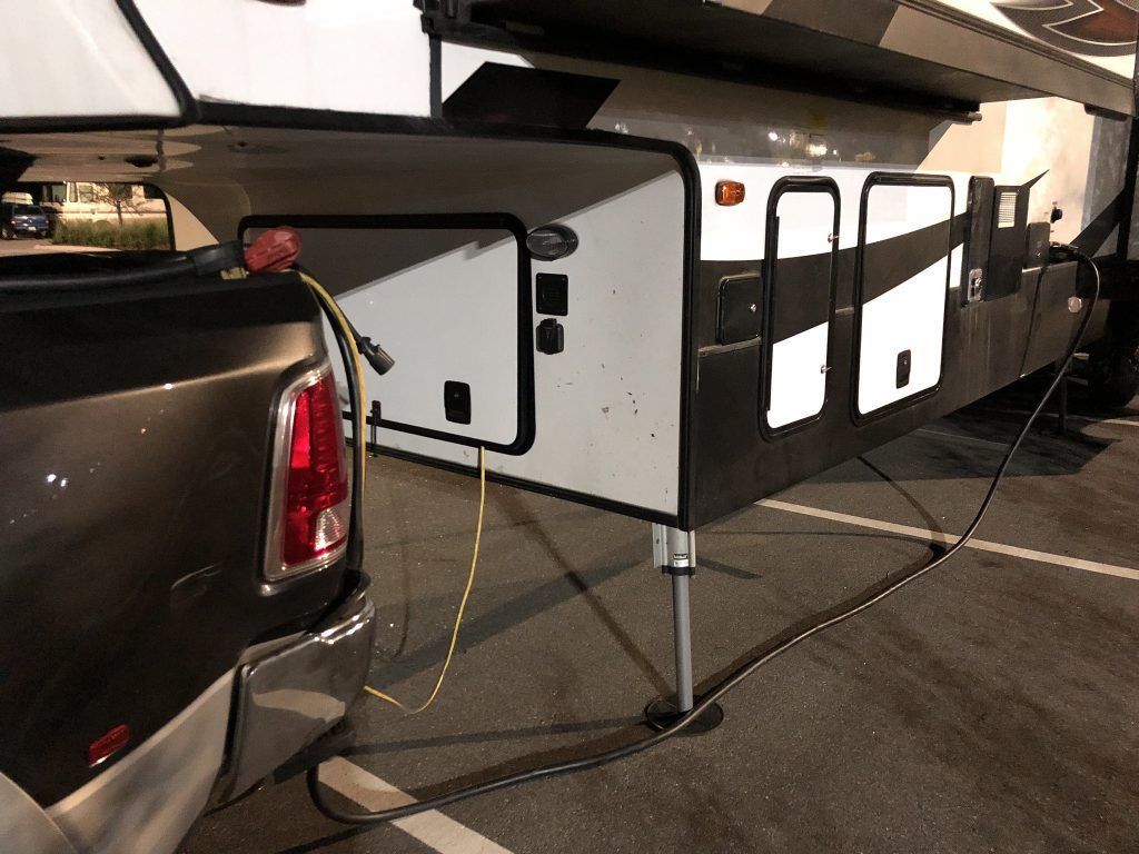 A truck is attached to a trailer with a cord coming out of the back.