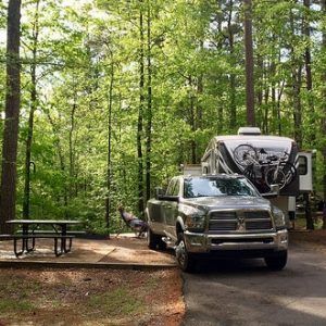A truck is parked next to a rv in the woods.