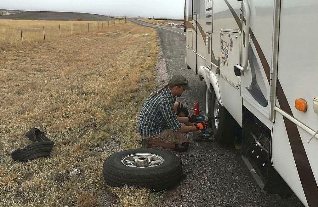 A man is changing a tire on the side of a rv.